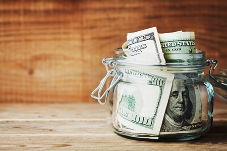 Jar of 100 dollar bills on a wood background